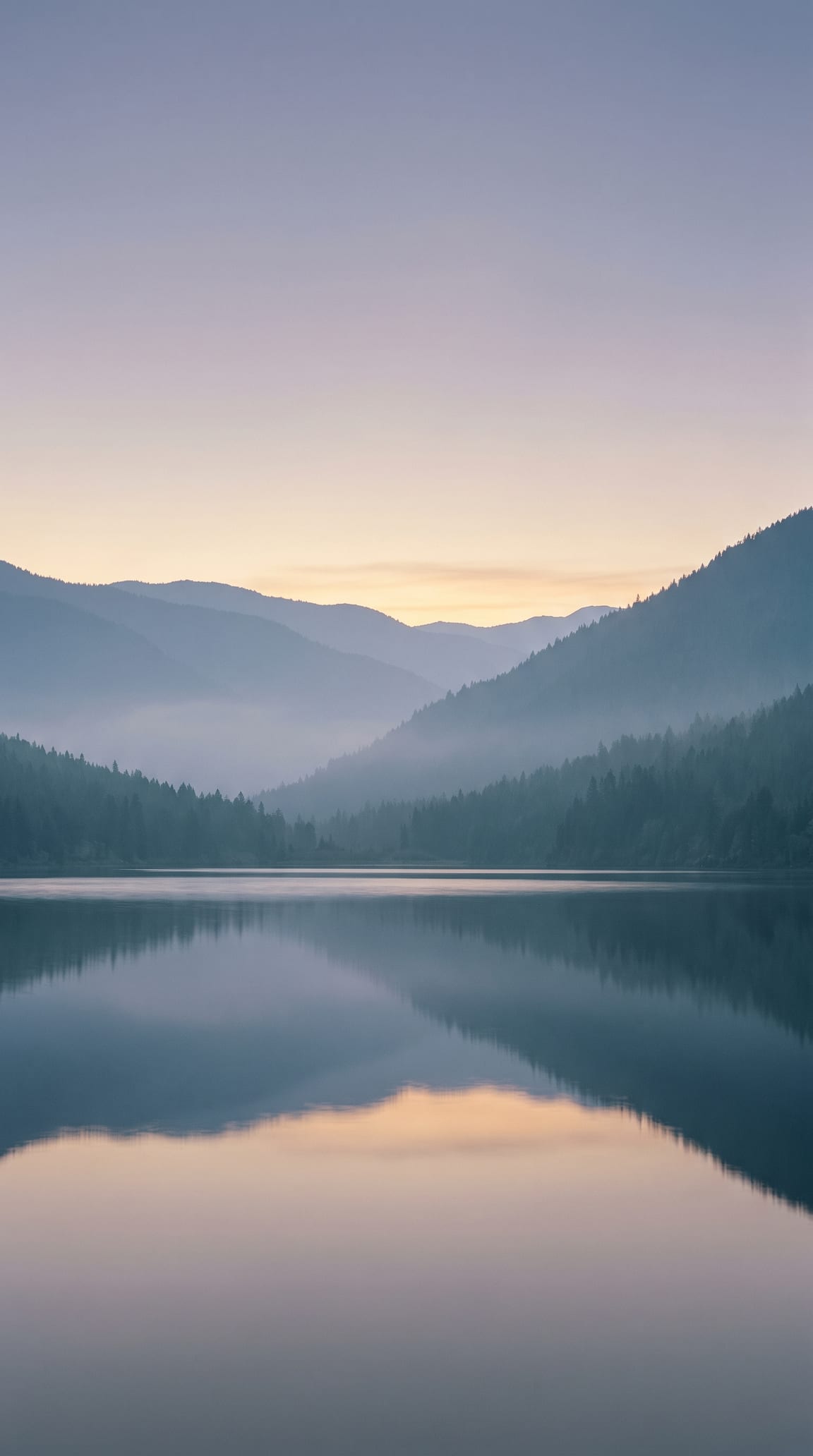 A Canadian valley at first light, mist lying between wooded ridgelines above a still lake holding the dawn sky
